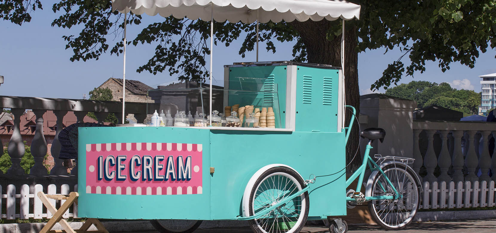 A teal ice cream cart with a custom ICE CREAM adhesive vinyl decal applied to the side for outdoor branding.